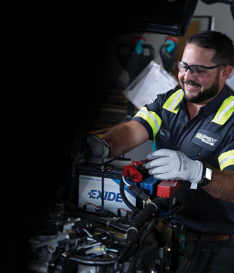 A smiling Equipment Depot service technician performing an inspection on a forklift battery.